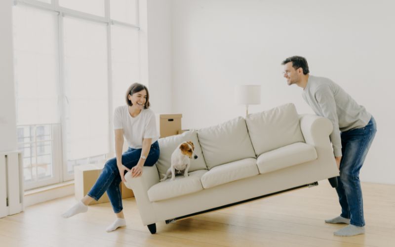 Man raising couch while woman and dog are sitting on it
